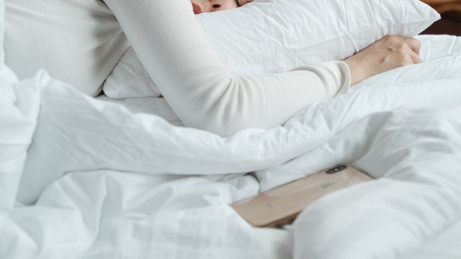 Woman in cozy bedroom sleeping peacefully, white bedding