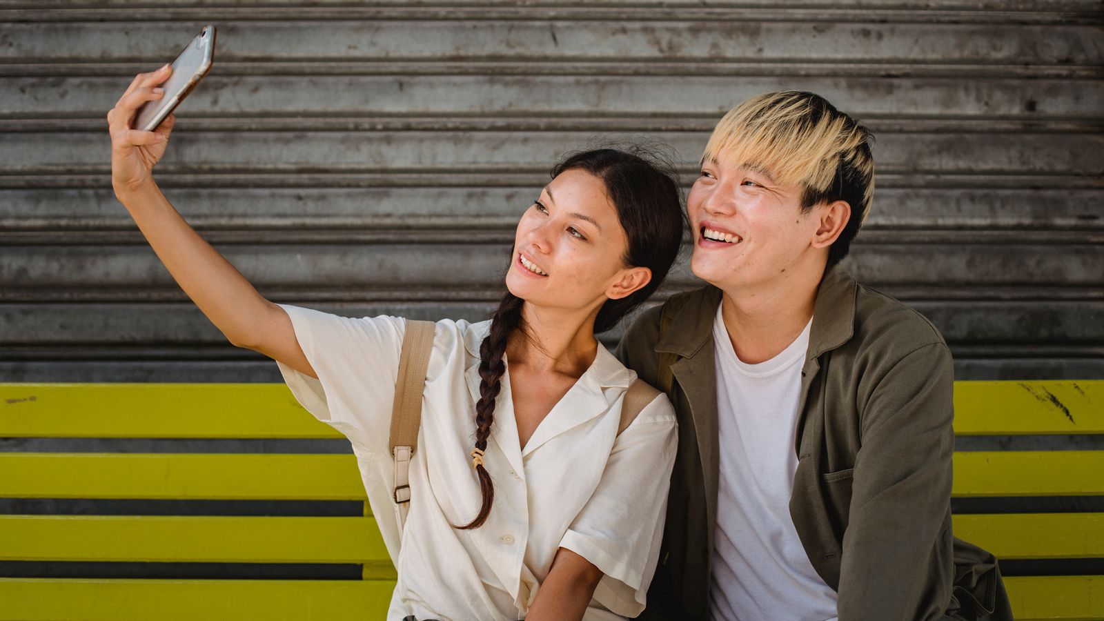 Asian couple taking selfie on smartphone on bench