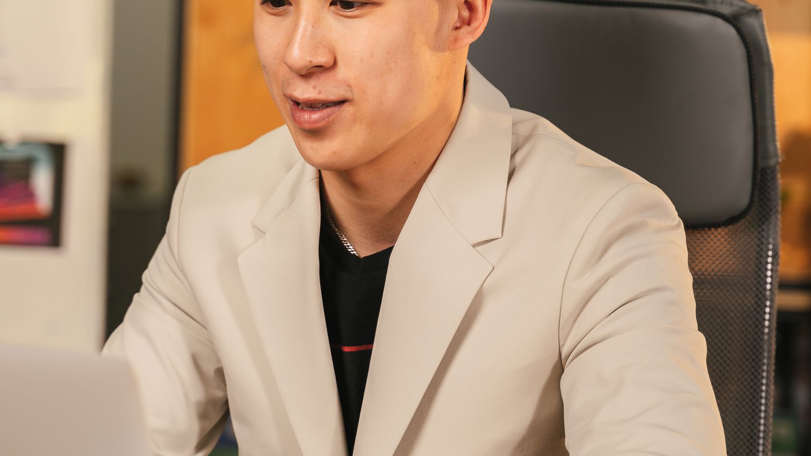 Asian man in white coat typing on laptop, wooden desk