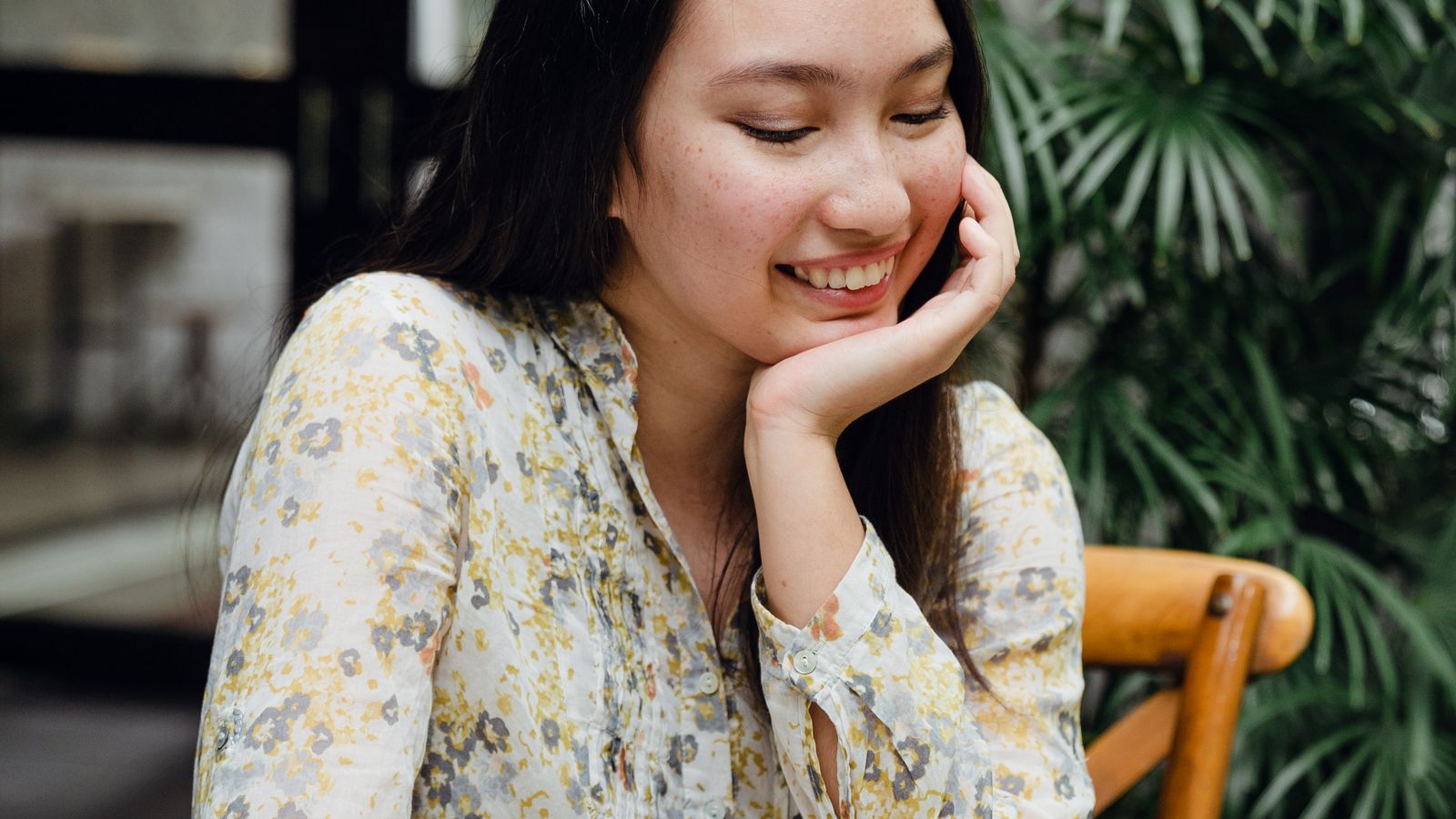 Smiling young Asian woman sitting in cafe with chin on hand