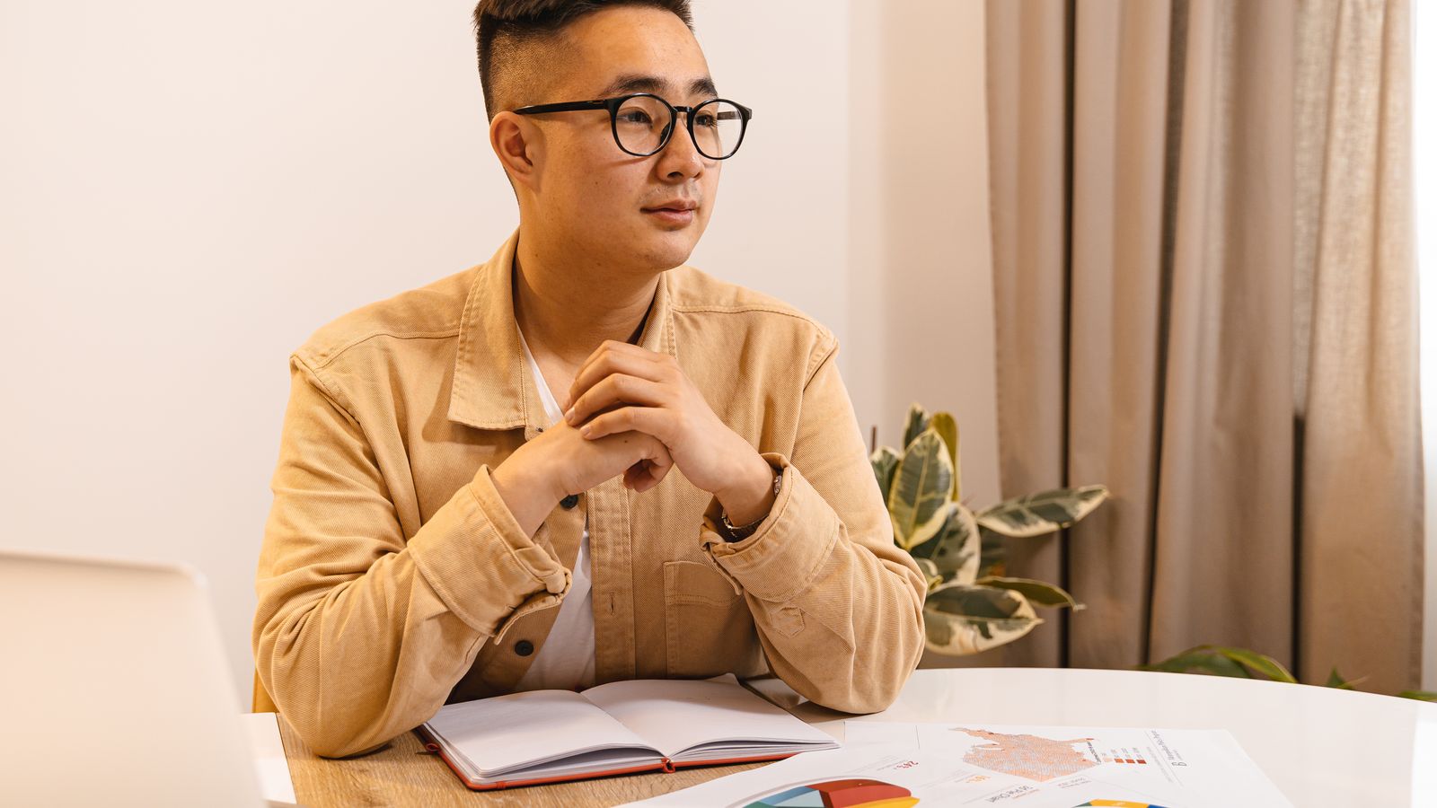 Asian man working at desk, documents and laptop, thoughtful