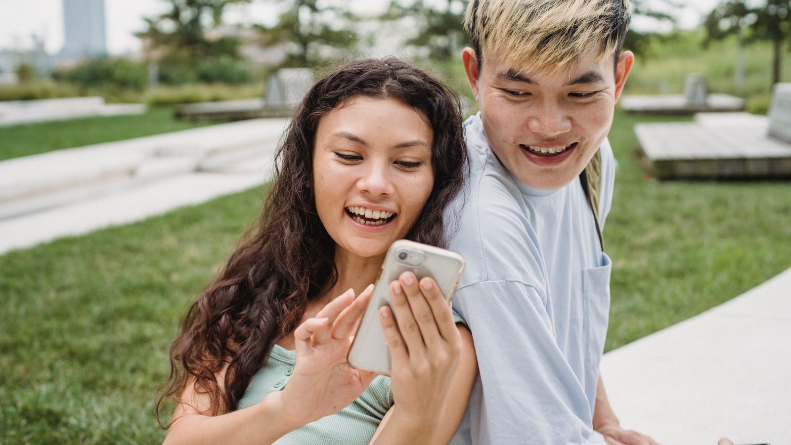 Ethnic woman sharing smartphone with Asian boyfriend