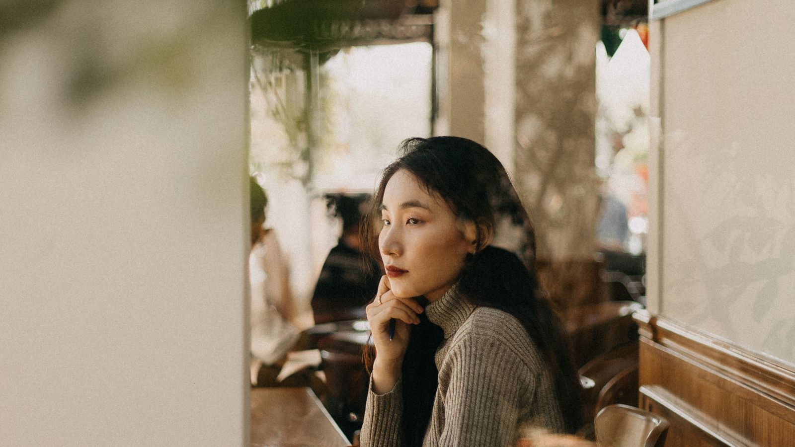 Woman sitting by window of cozy cafe, thoughtful serene