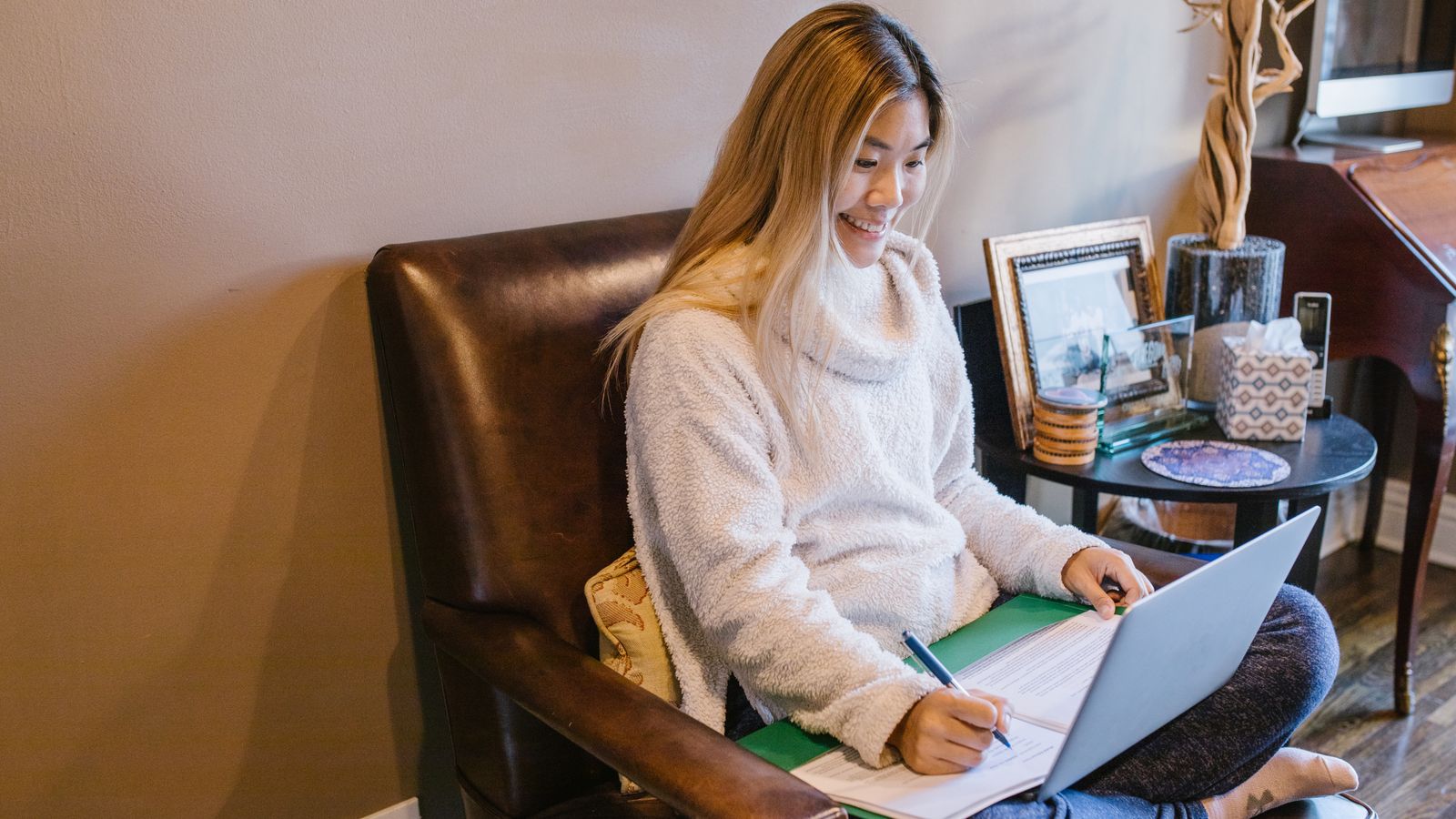 Asian woman writing notes, laptop, cozy home