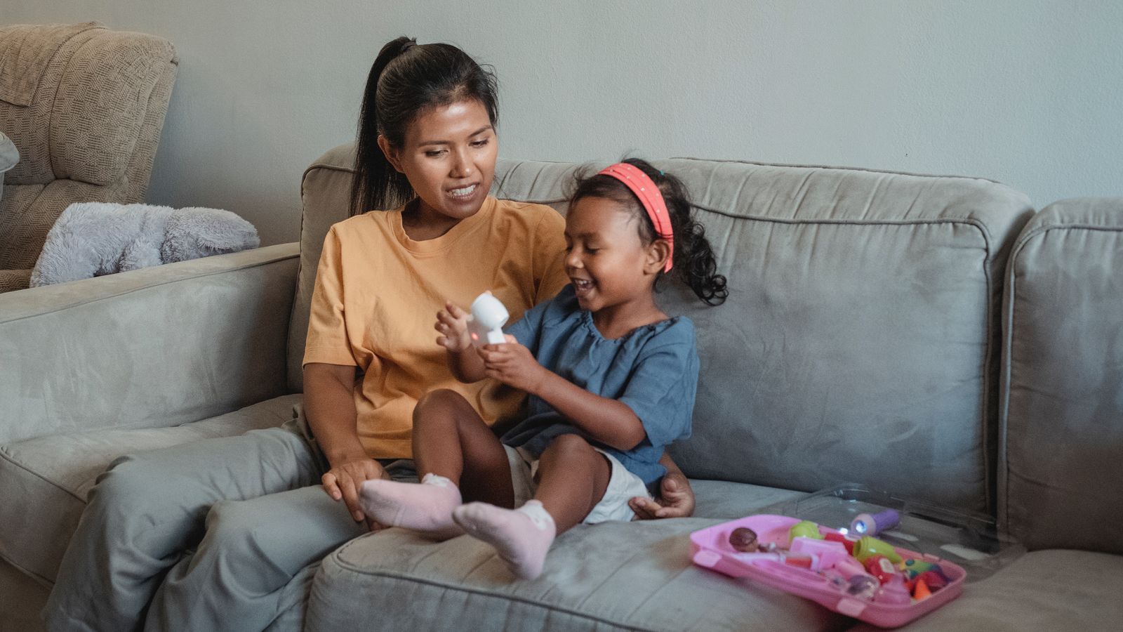 Asian mother and daughter with toy on sofa