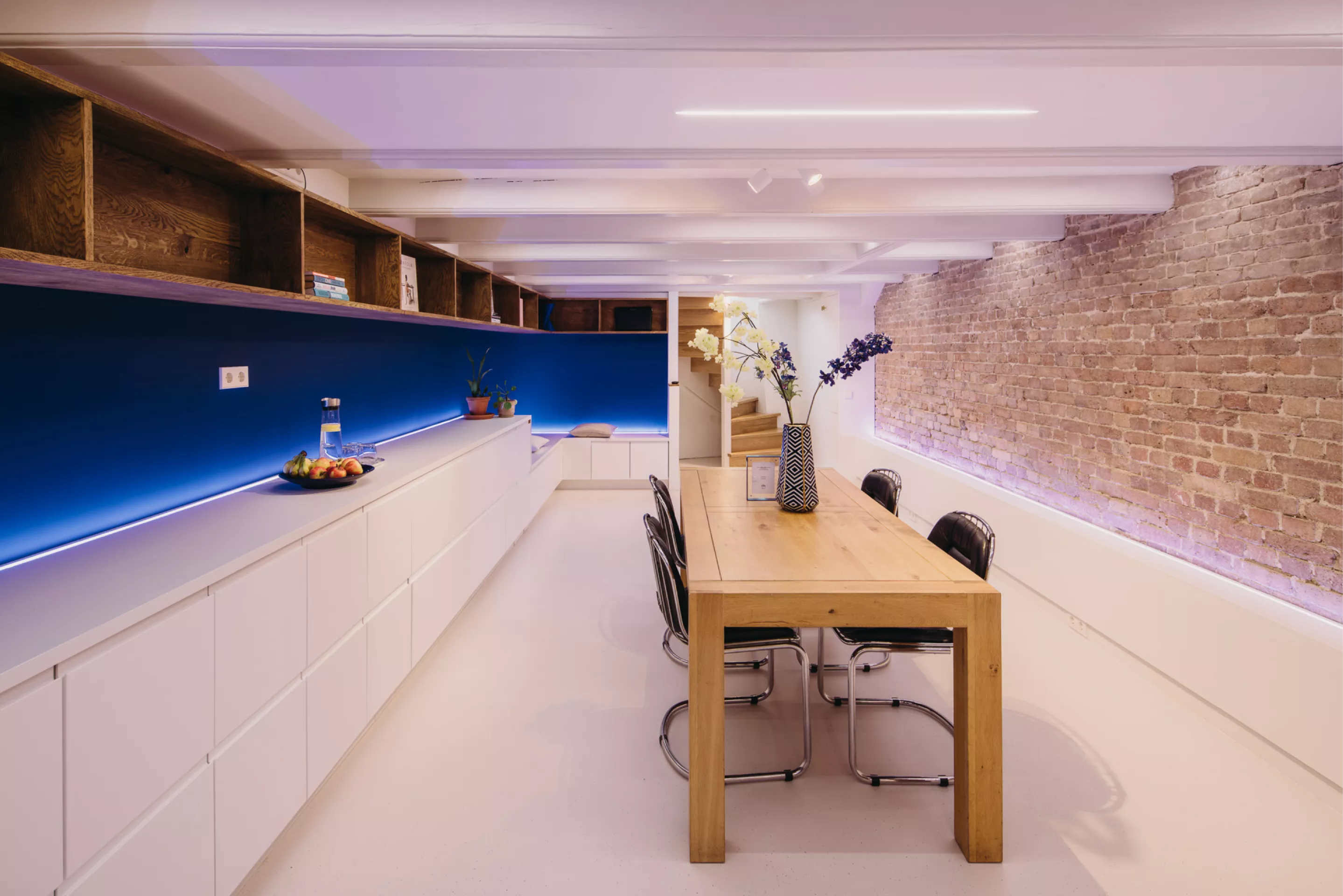 Brede blik op KW9 souterrain: vergadertafel tussen baksteenmuur en moderne blauwe mediawand