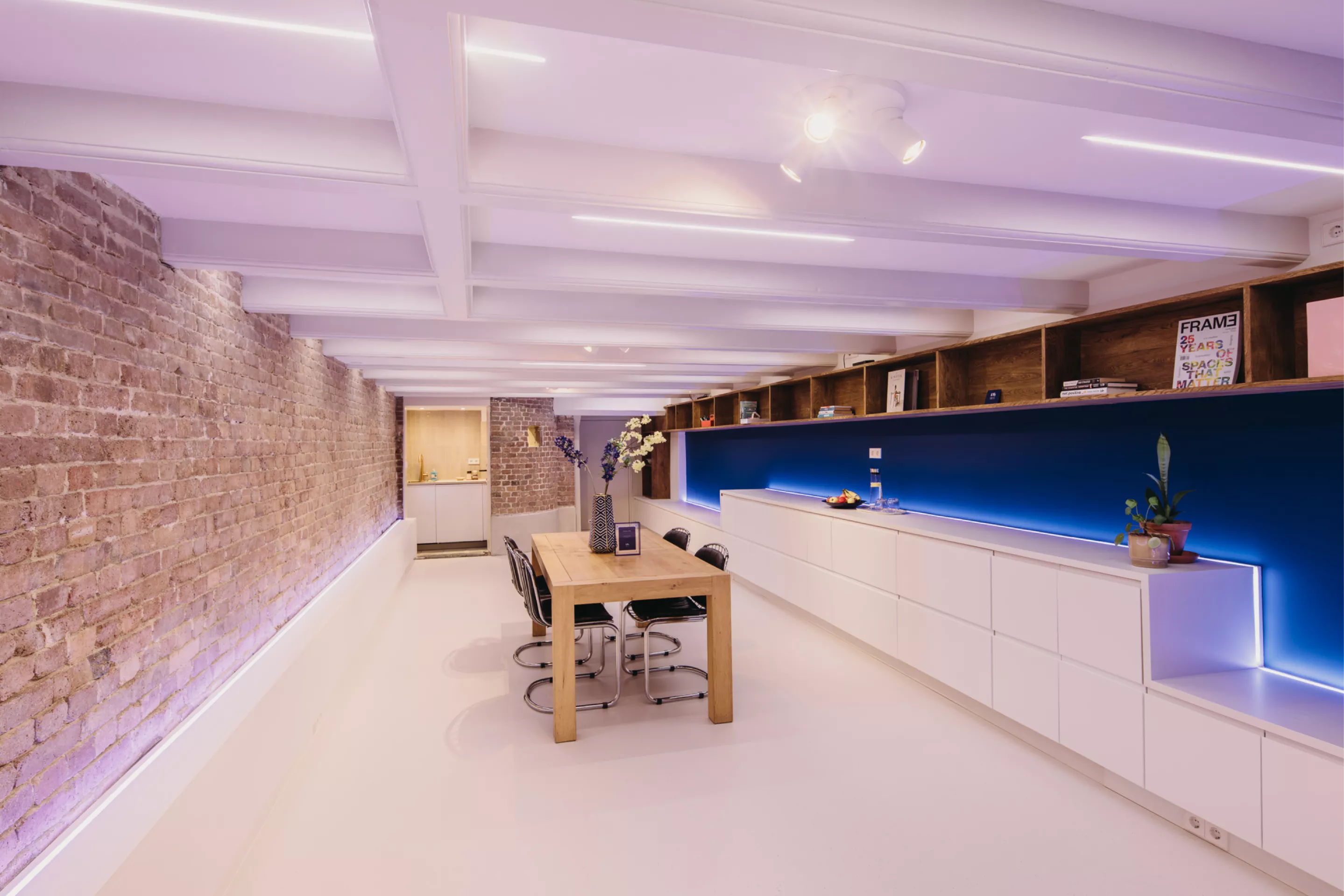 Vergaderruimte in het souterrain van KW9 met lange houten tafel, bakstenen muur en modern blauw verlicht paneel