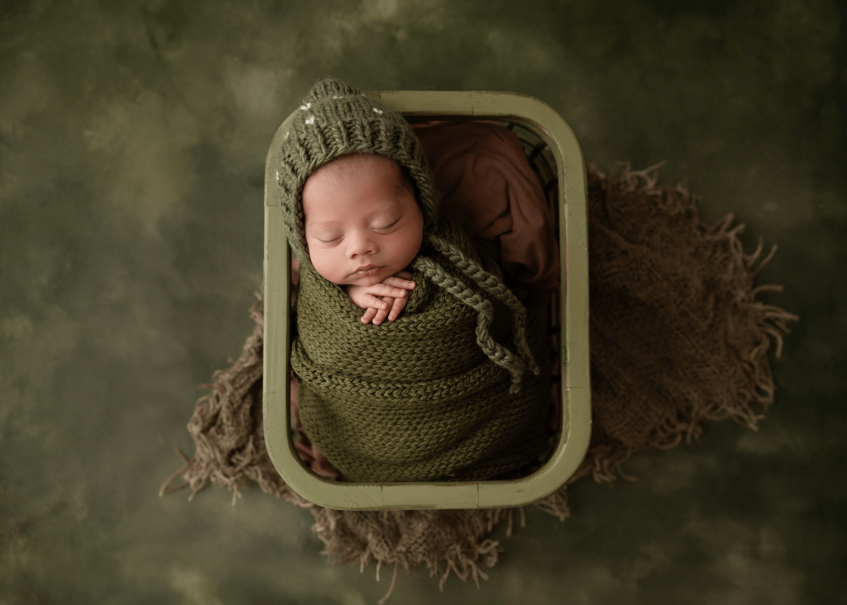 a sweet baby boy all in brown sleeps in a brown basket on a brown background for newborn pictures billings mt

