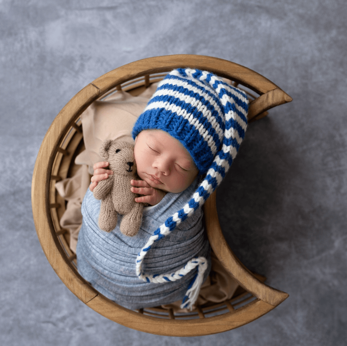 a baby boy sleeps in blue blanket inside of a moon shaped basked for newborn photography session billings mt