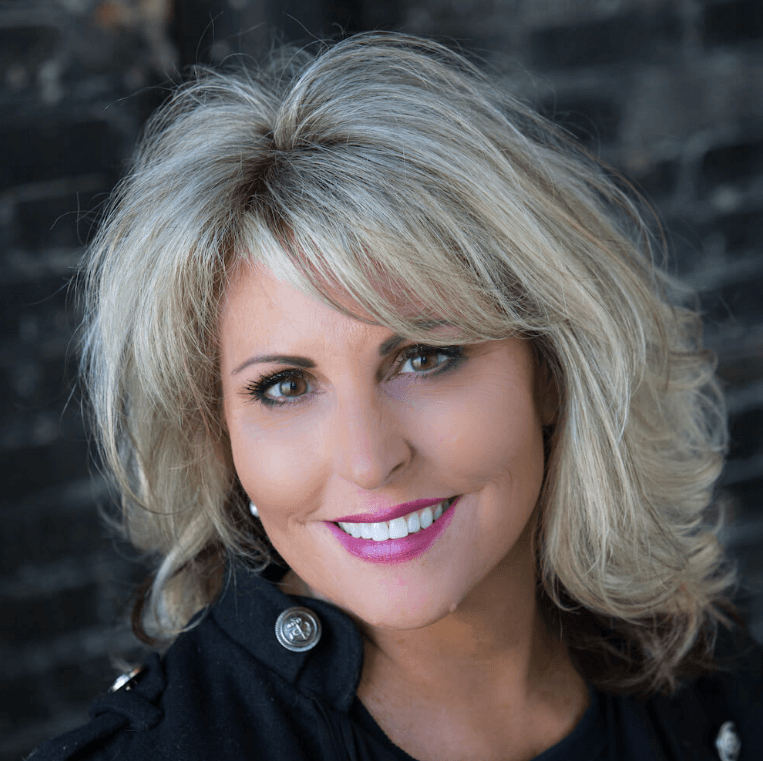 female real estate agent smiles at camera in front of brick wall commercial headshot square