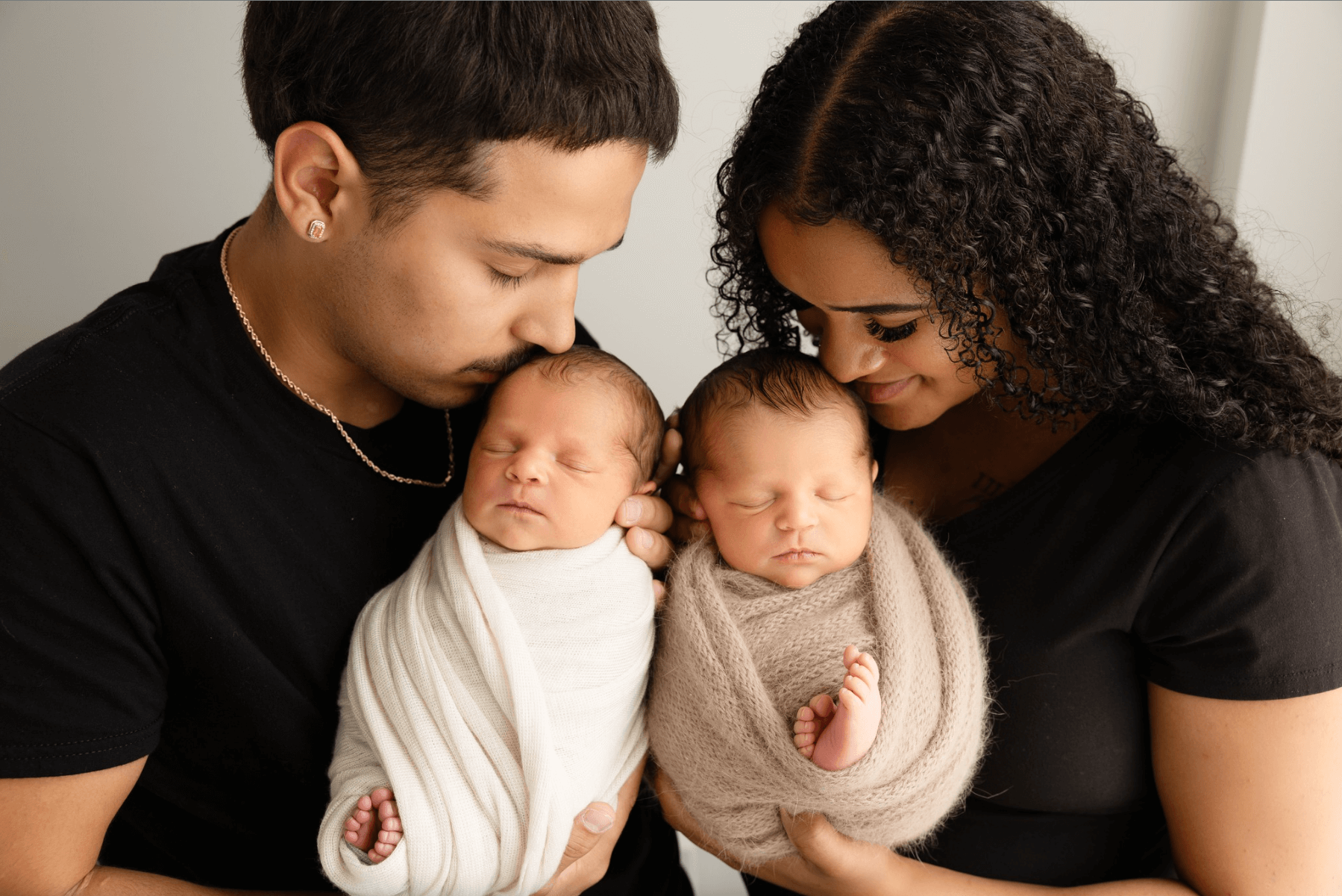 newborn twins held by their biracial mother and father. a baby girl sleeps in a studio wicker basket. a cute older sister lovingly snuggles her sleeping newborn brother. best newborn photographer in Billings MT