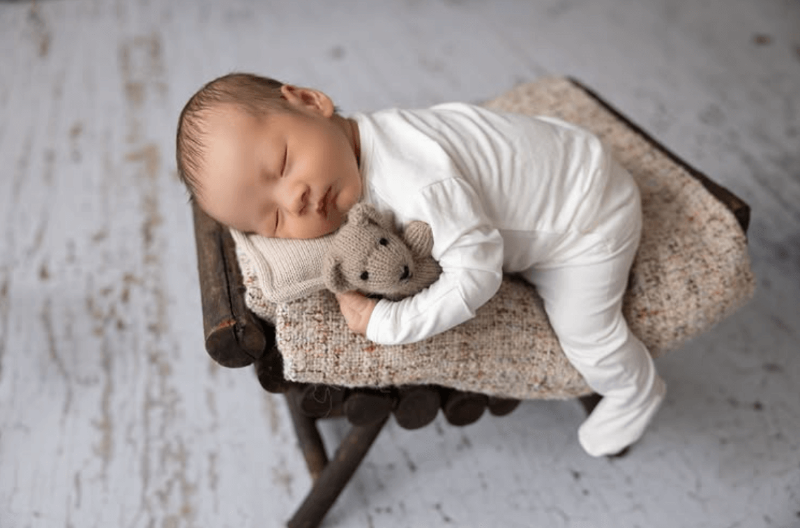 a cute baby boy lounges on a little wooden bench while clutching a stuffed animal. a baby girl sleeps in a studio wicker basket. a cute older sister lovingly snuggles her sleeping newborn brother. best newborn photographer in Billings MT