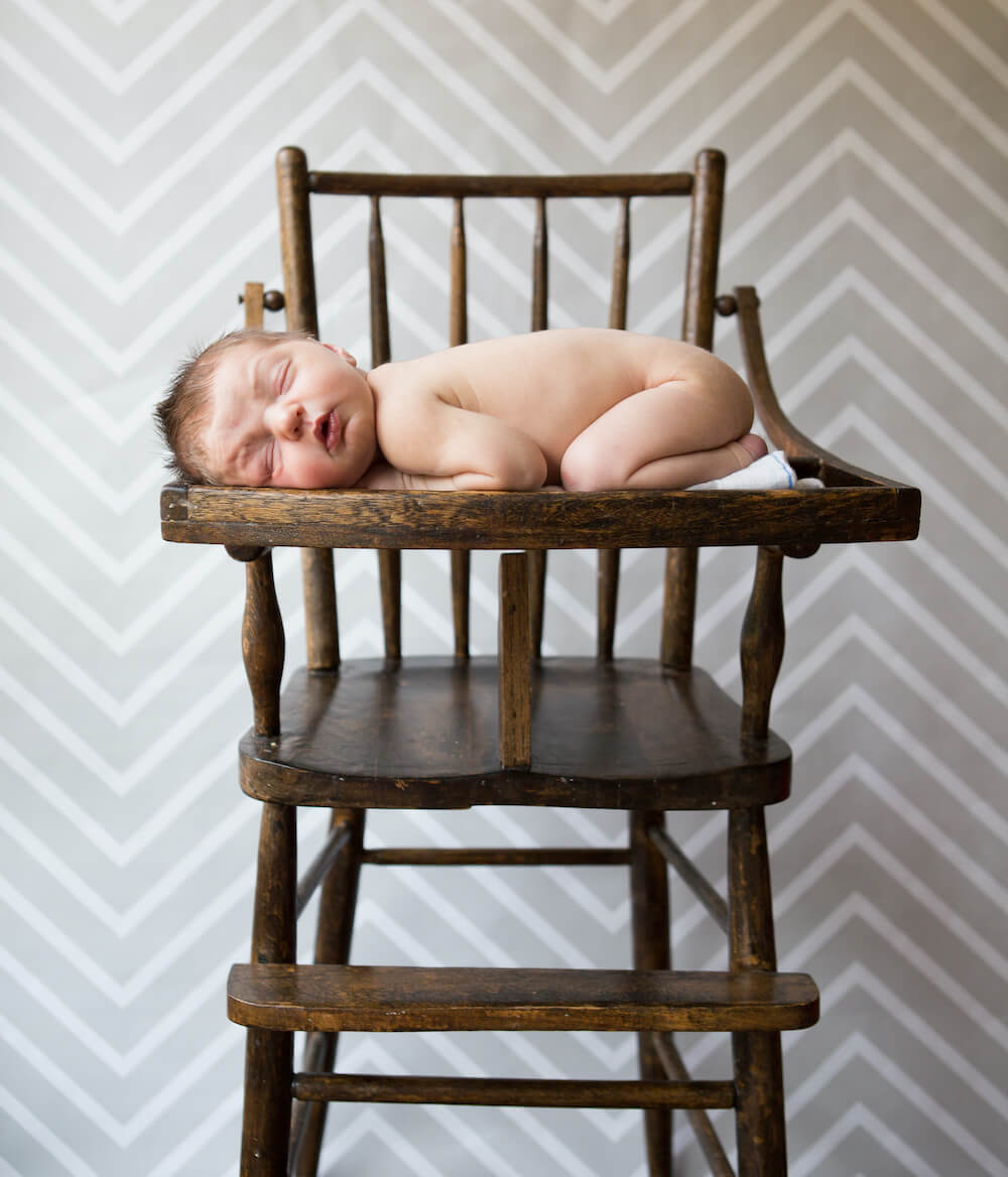 Newborn Sleeps on High Chair in Photography Studio
