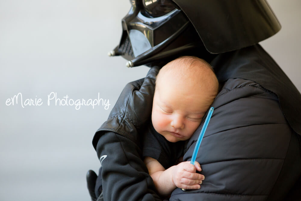 Dad dressed as dark star lord Holds Newborn baby boy with tiny lightsaber