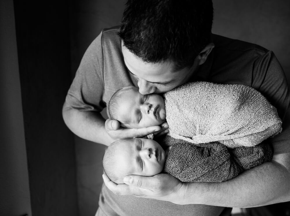 Dad kissing twin newborns