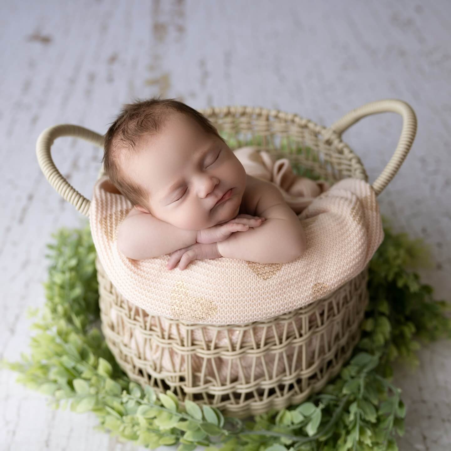 newborn rests on crossed arms in a basket with greenery around