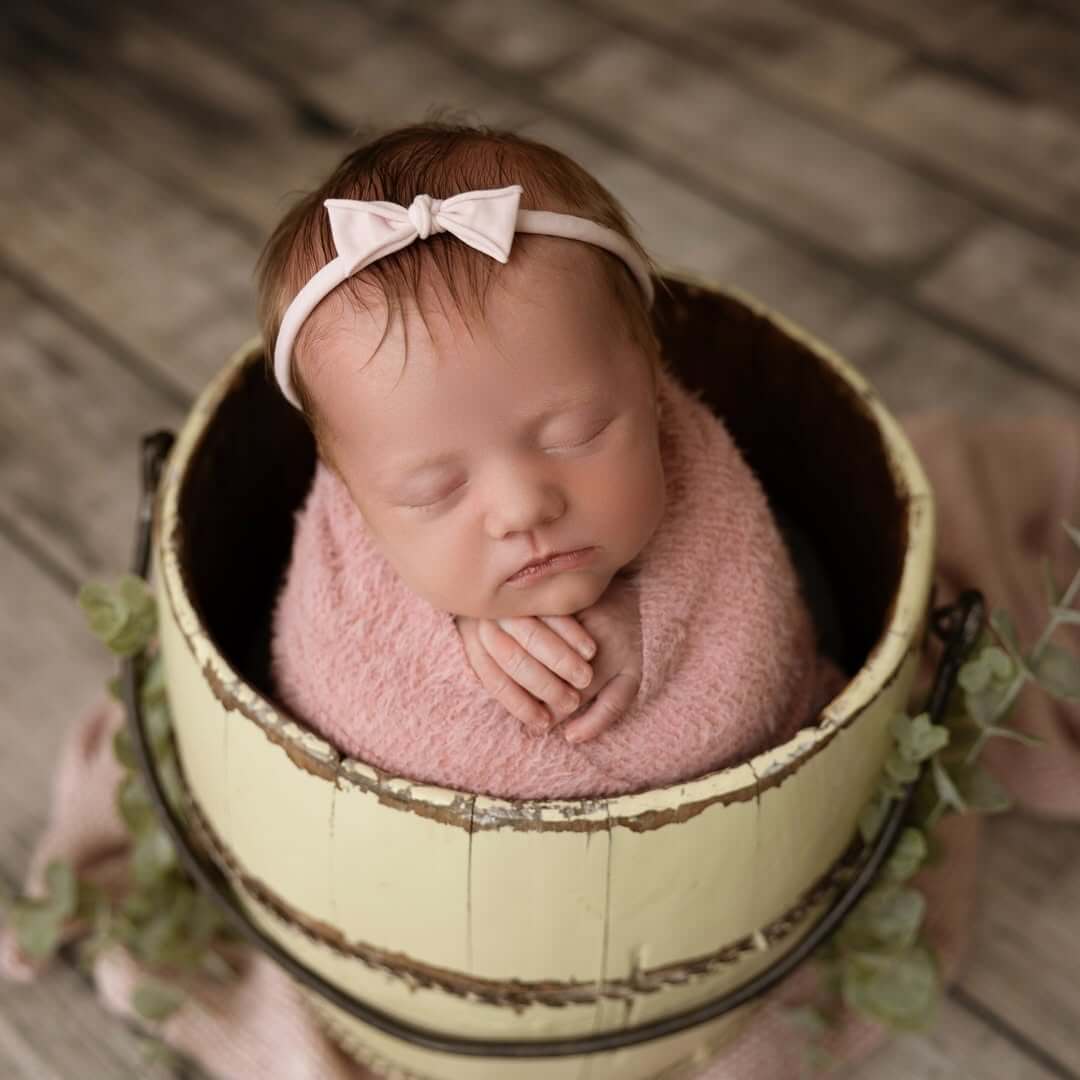 cute baby girl in bow sleeps in a wooden barrel  newborn photography in billings mt