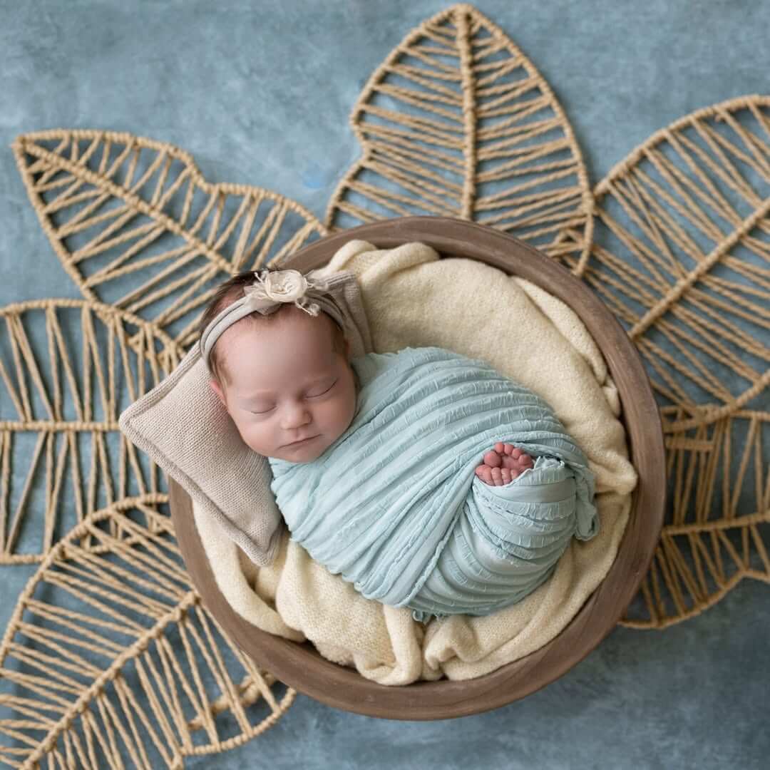 baby girl sleeps in swaddle and toes sticking out on a palm frond background in billings photography studio