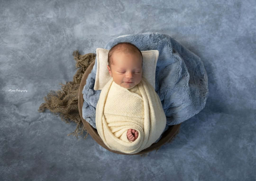 tiny newborn baby boy sleeps on a background of blue with toes poking through the blanket newborn photography billings mt