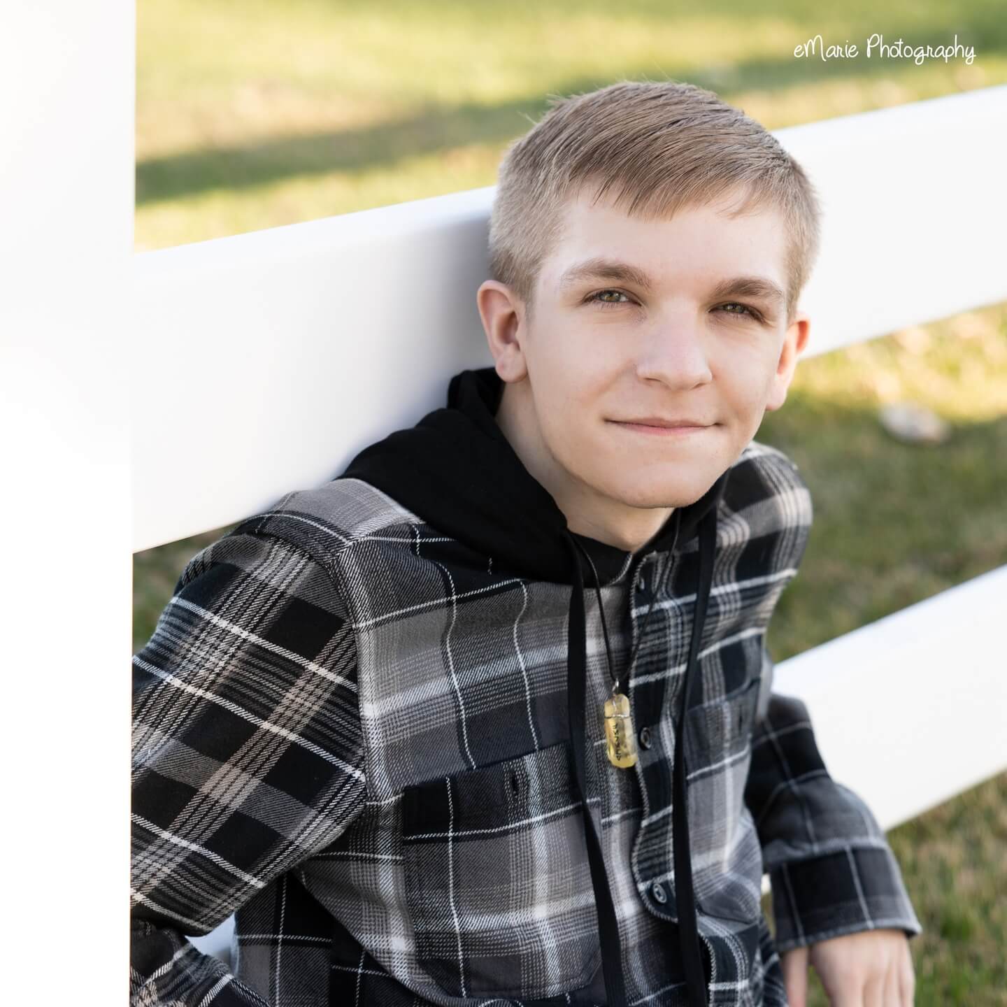 high school senior boy rests outside against a white fence and smirks at the camera