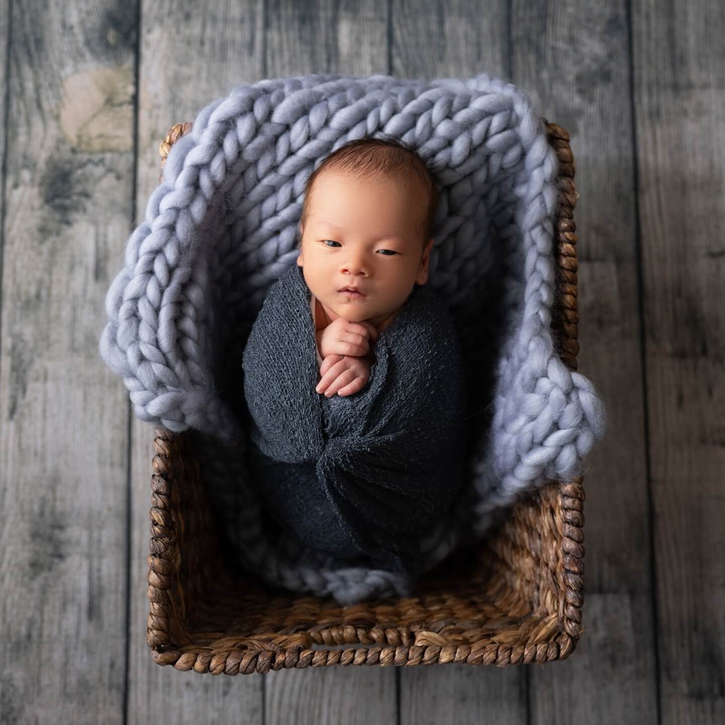 newborn baby looks at camera in blue blanket and wicker basket newborn photography billings mt