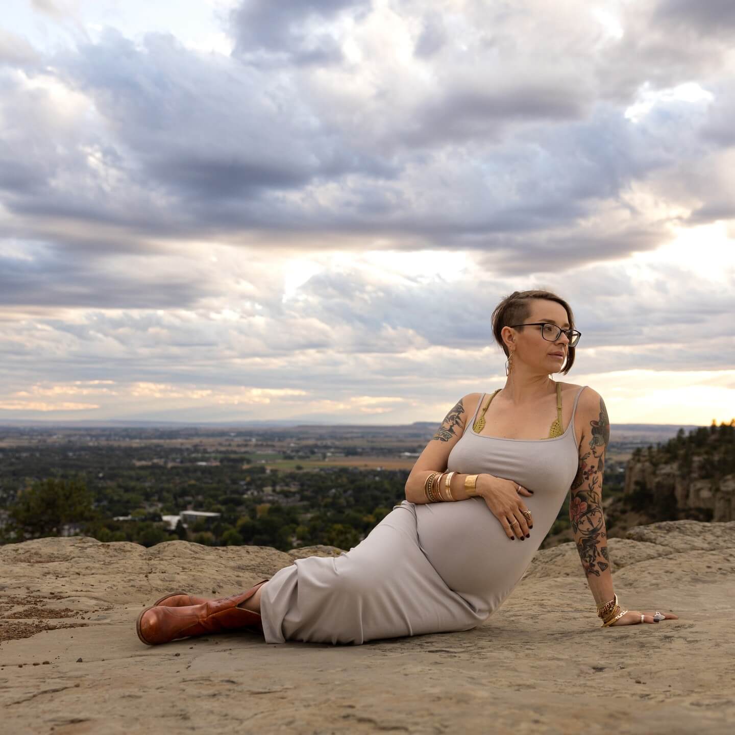 tattooed pregnant woman looks to the side on top of the rimrocks overlooking billings mt