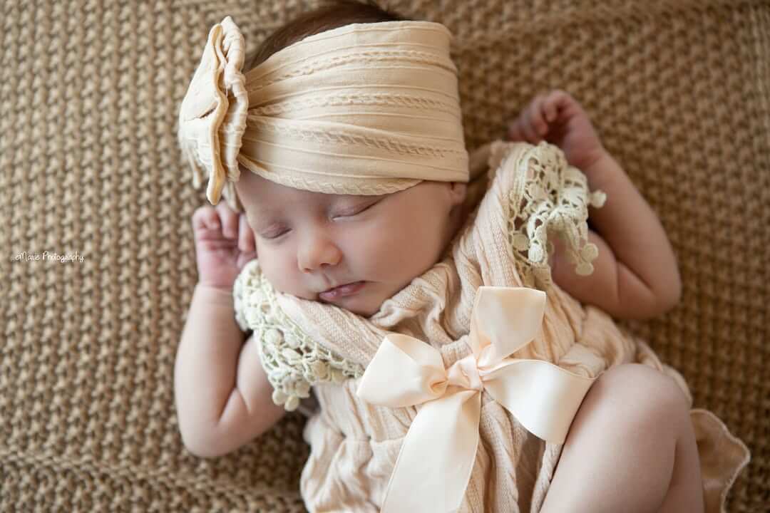 in home newborn baby girl sleeps on family  knitted brown blanket with brown bow
