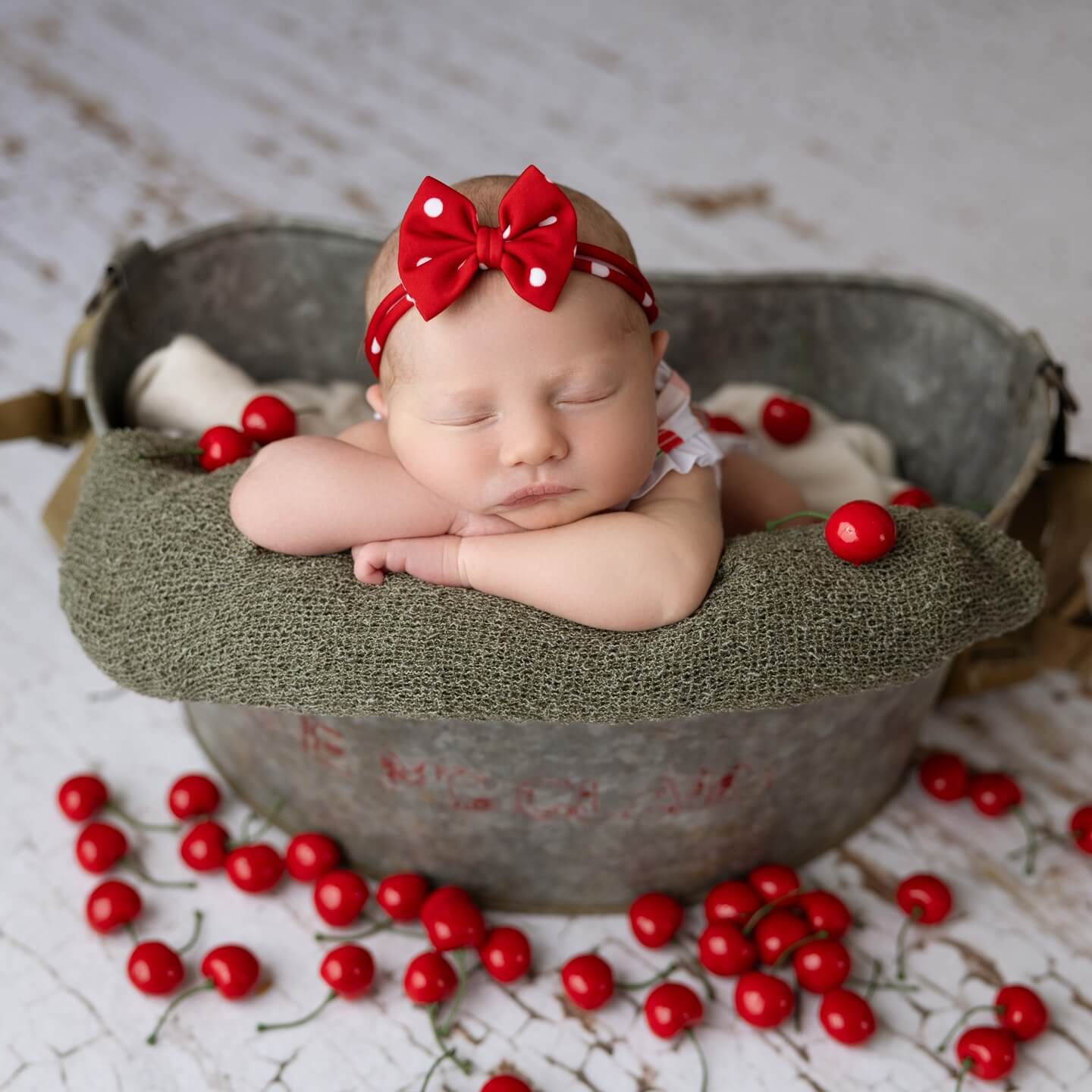 cute little newborn baby girl in red bow in basket with cherries around newborn photography billings mt