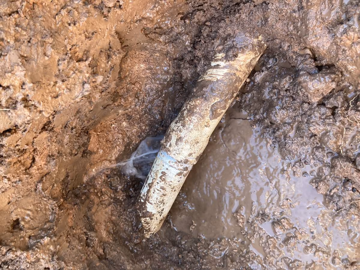 Corroded water main leaking in a muddy trench — the kind of aging infrastructure that drives capital budget decisions