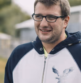 Smiling man wearing glasses and a blue and white zip-up hoodie outdoors.