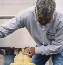 Man in gray Water Corporation sweatshirt inspecting or operating a yellow fire hydrant.