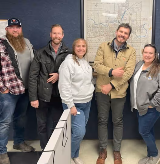 Five people smiling and standing together in an office setting with a map on the wall behind them.