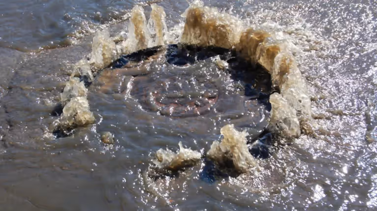 Water main break with water erupting from underground pipe requiring emergency utility repair