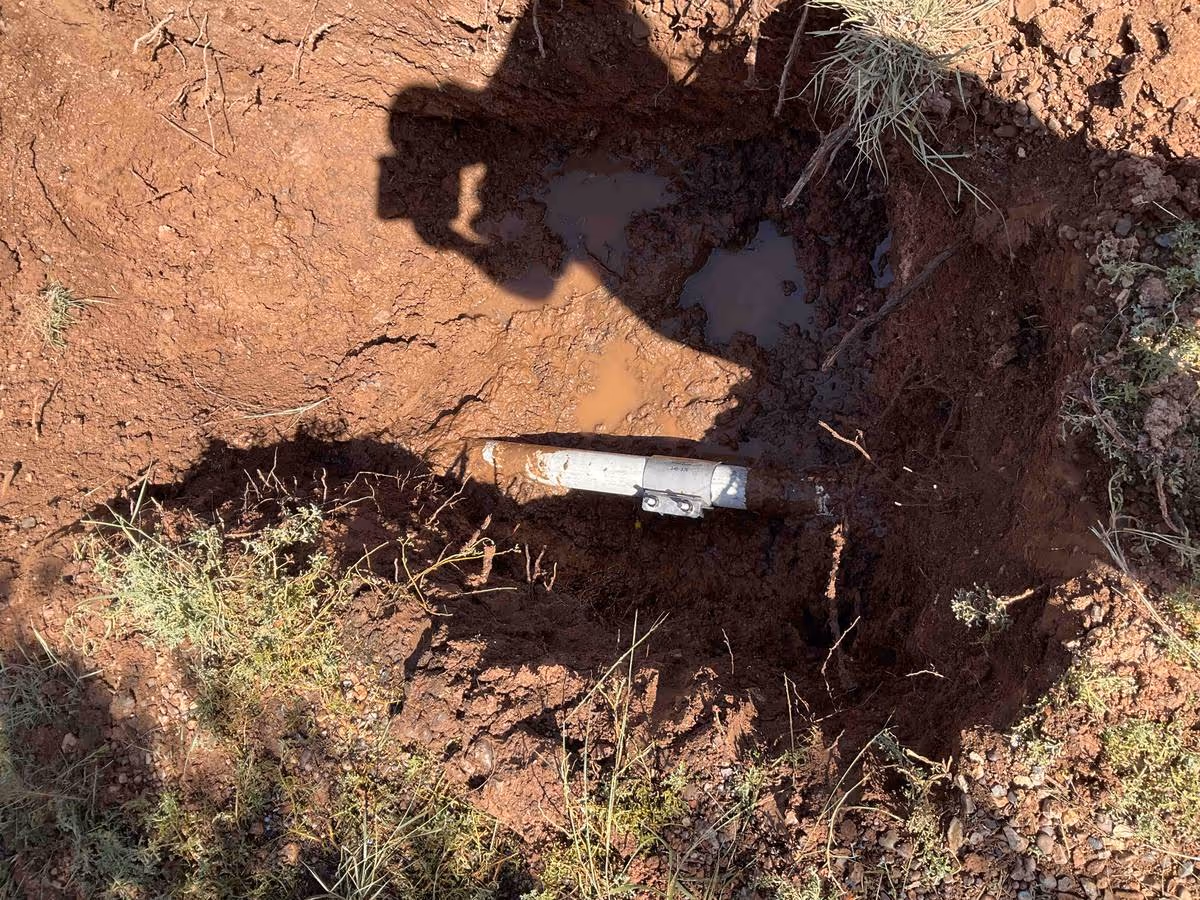 Buried water pipe partially uncovered in red clay — the infrastructure operators are trying to find