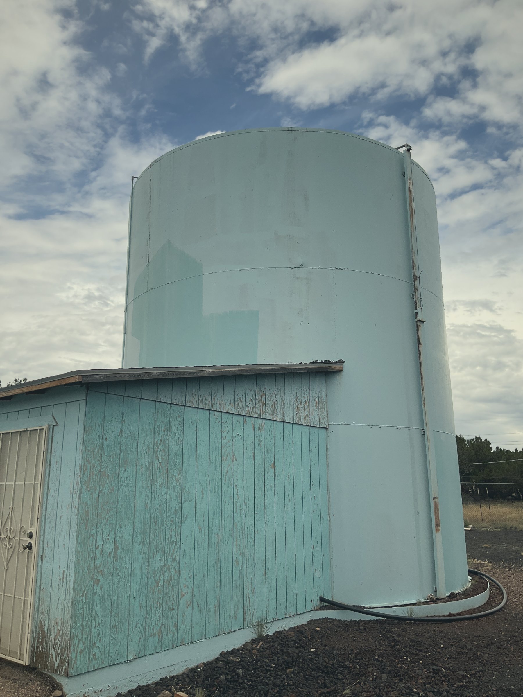 Water storage tank beside a small white shed at a rural well site