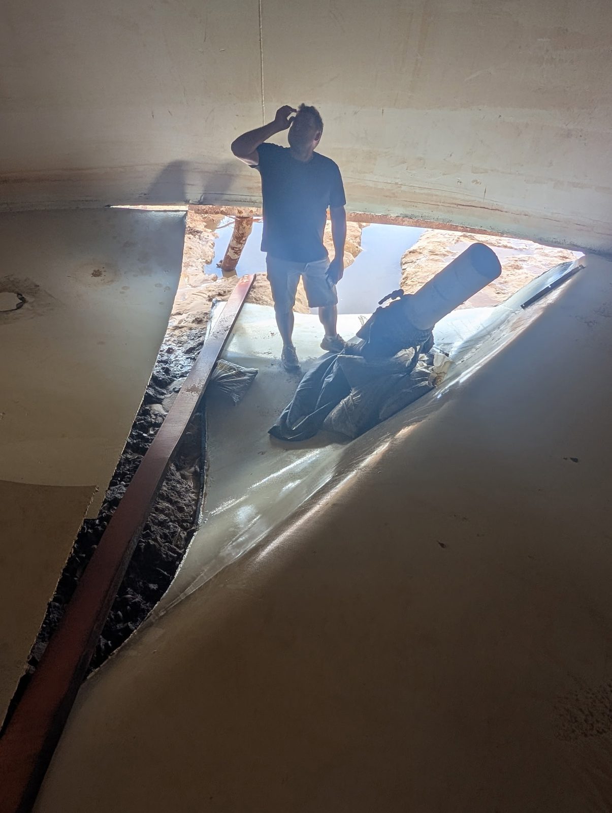 Inside the failed Heber DWID storage tank: the steel floor torn open along its seams, with a person standing on it for scale.
