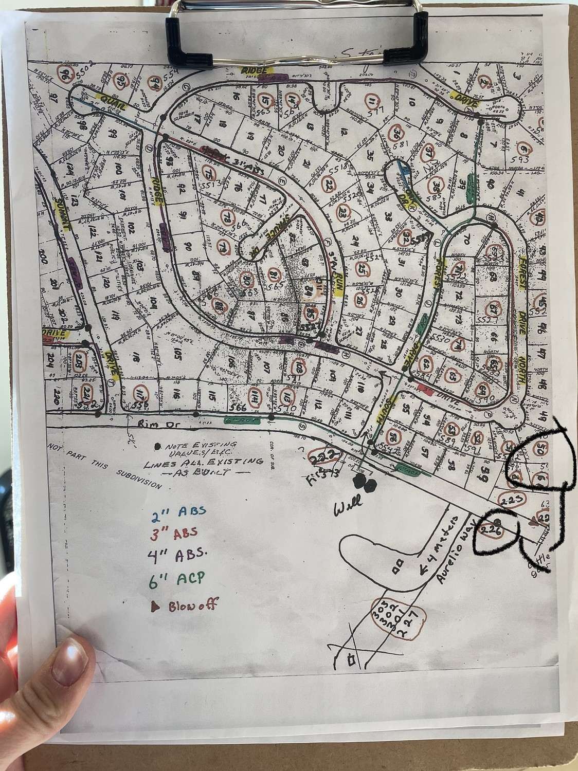 A county plat map of Pinedale Estates held on a clipboard, with the water system's mains, valves and blow-offs drawn on it by hand in marker.