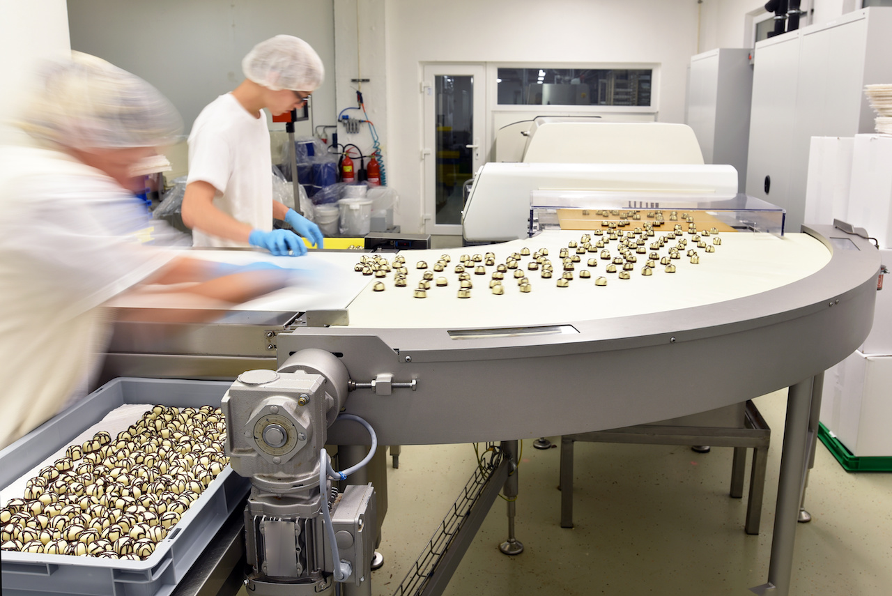 a person in a white robe and blue gloves working on a conveyor belt