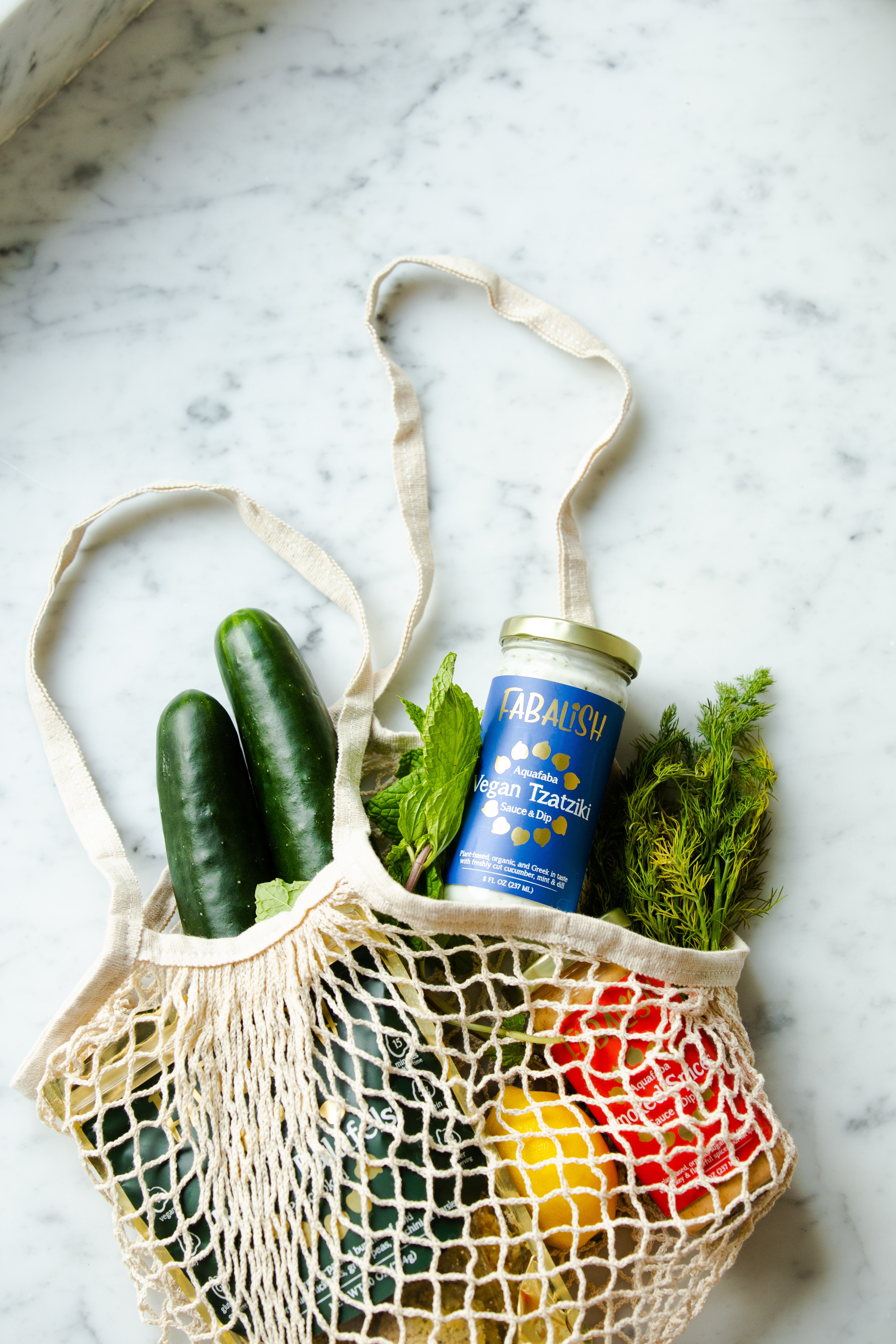 a string bag with vegetables and a jar of yogurt