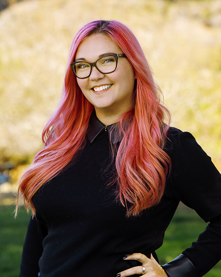 a woman with pink hair and glasses smiling