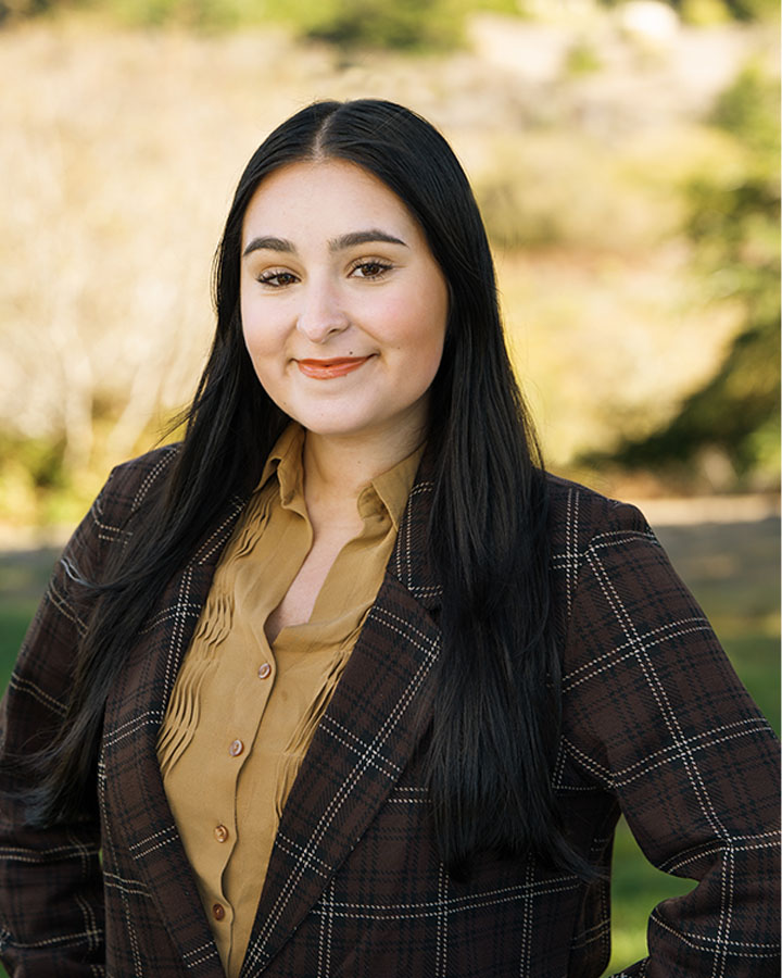 a woman with long black hair wearing a brown plaid jacket