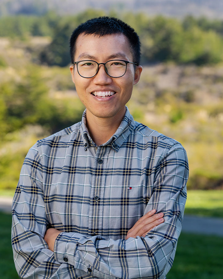 a man with glasses smiling with arms crossed