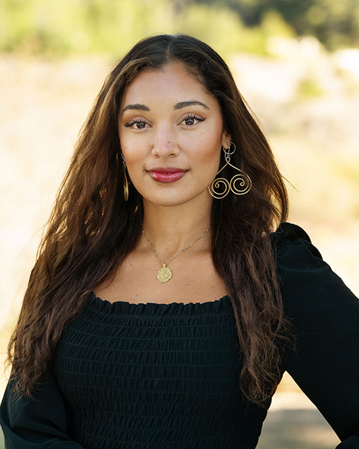 a woman with long hair wearing a black dress and gold earrings
