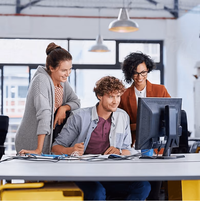 Three coworkers smiling and looking at a computer screen in a modern office.