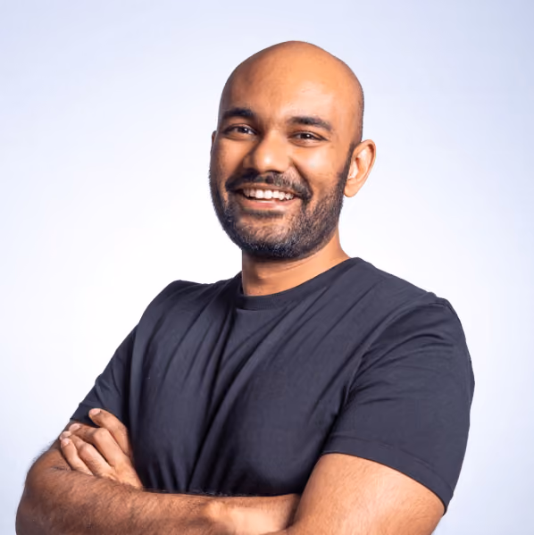 Smiling bald man with beard, wearing a black t-shirt, arms crossed against a light background.