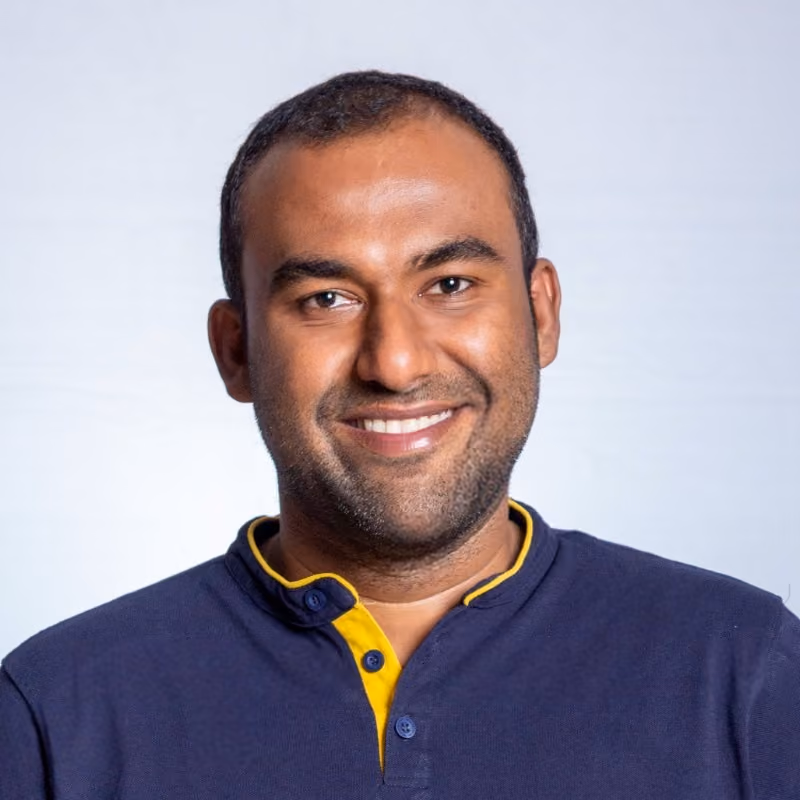 Smiling man with short hair wearing a navy blue and yellow collared shirt.