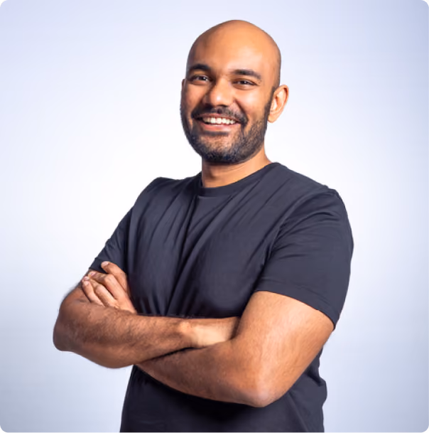 Smiling bald man with beard crossing arms, wearing a black t-shirt on light background.