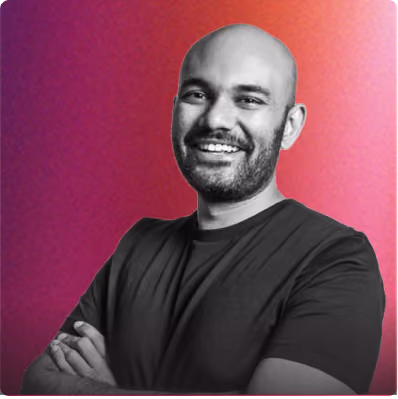 Smiling bald man with a beard wearing a dark t-shirt against a pink and purple gradient background.