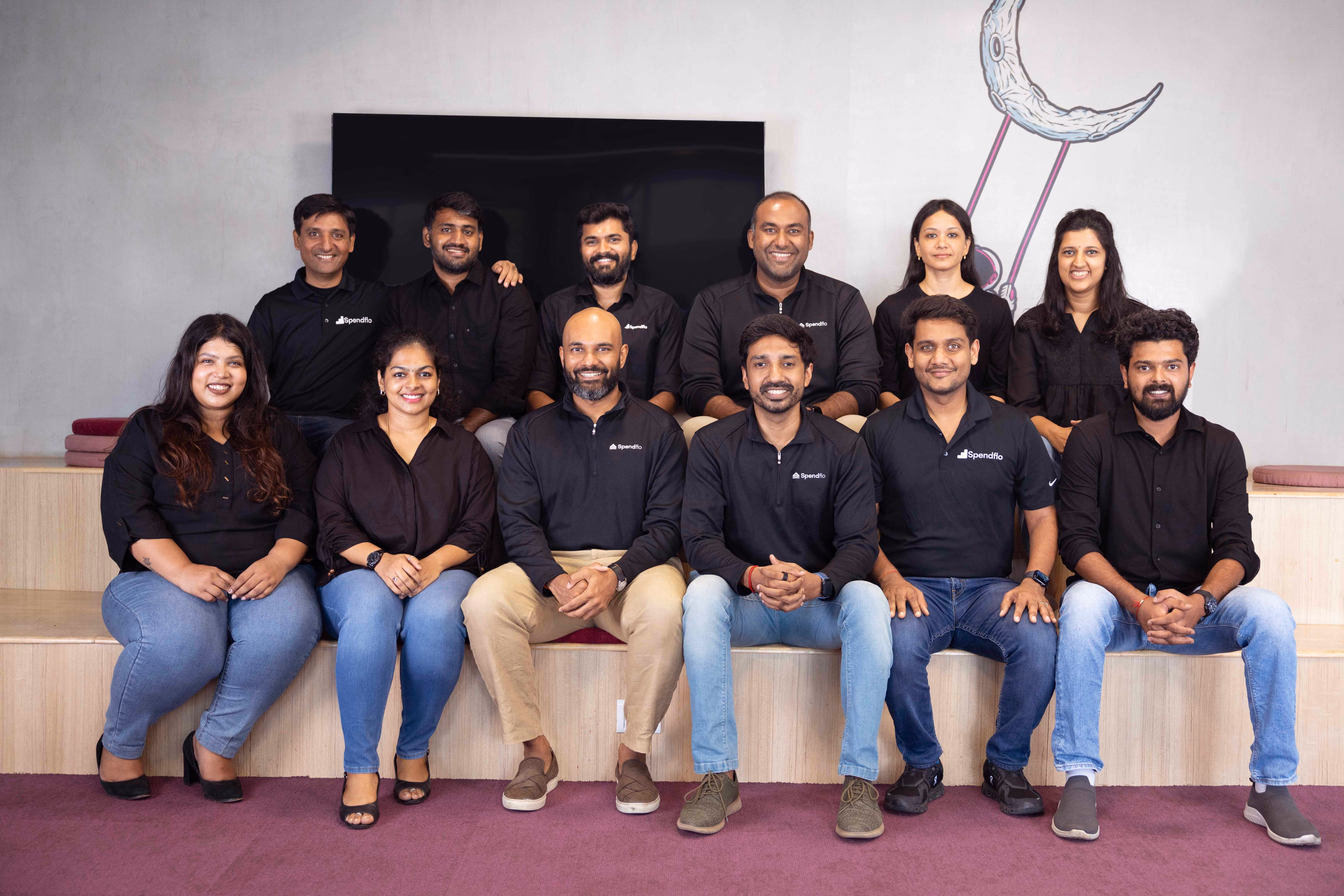 Group photo of eleven people sitting and standing indoors, many wearing Spendflo branded shirts.