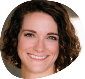Photo of Stacy Branham, asymmetrical brown wavy hair and a big smile, with a fancy bookshelf in the background.